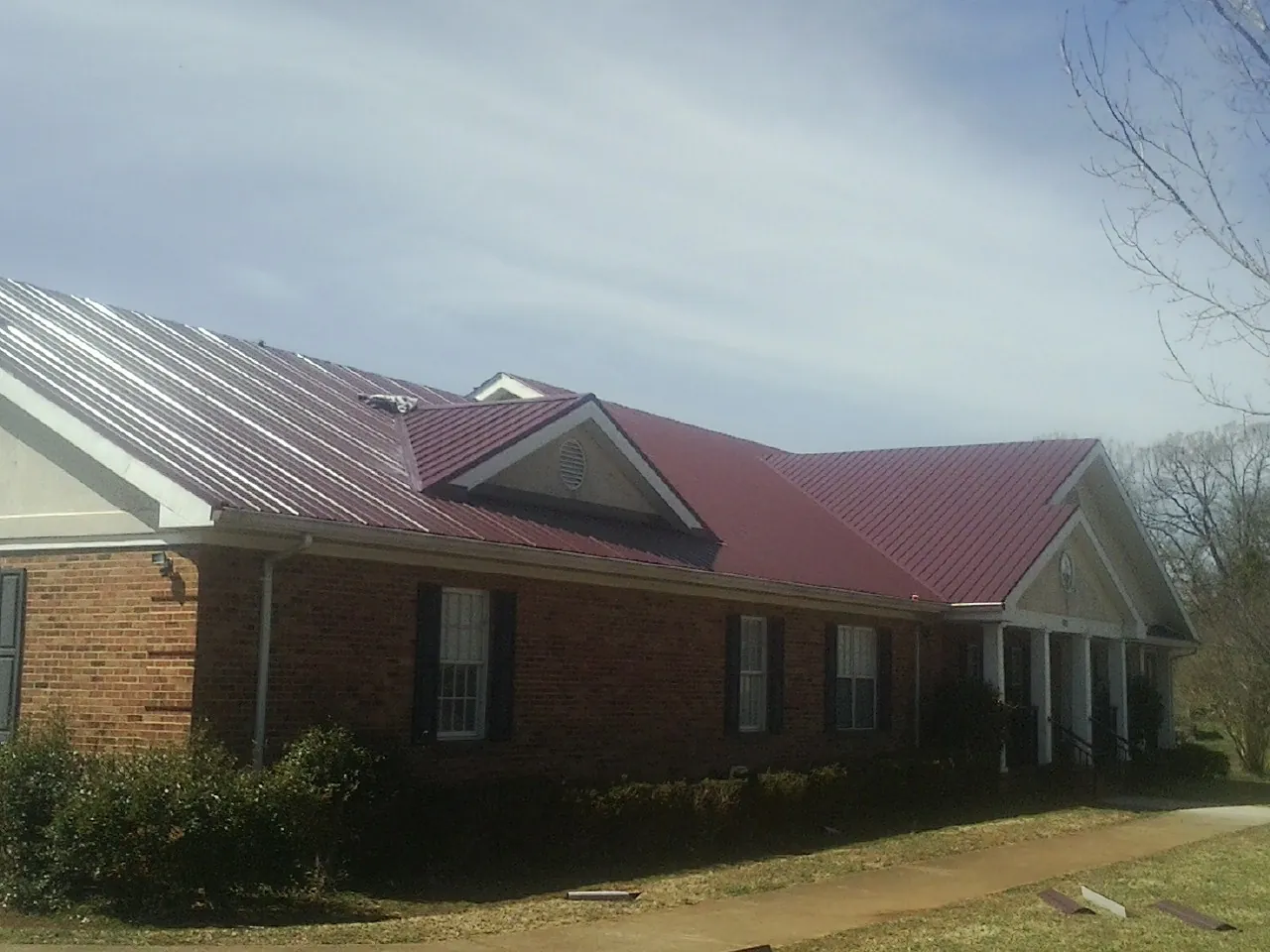 Red metal roof with gabled entries on a long brick building, from a Hail Damage Roof Repair job in Naval Air Station Jrb