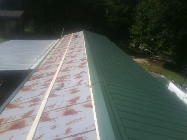 Old rusted panels beside newly installed green metal roofing — Wind Damage Roof Repair by Roofing Brothers in Naval Air Station Jrb