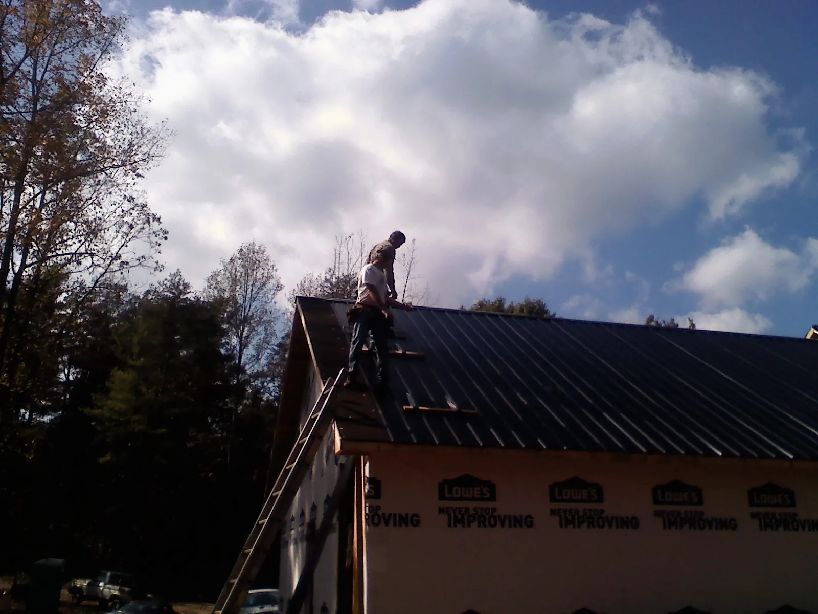 Roofer fastening dark metal panels high against a cloudy sky, from a Roof Inspection job in Naval Air Station Jrb