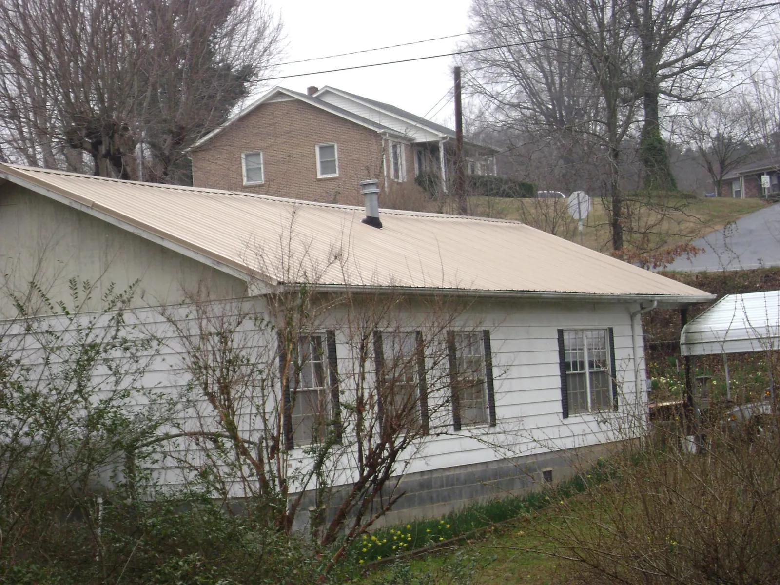 Tan metal roof on a white sided house set into a hillside — Commercial Roofing by Roofing Brothers in Naval Air Station Jrb